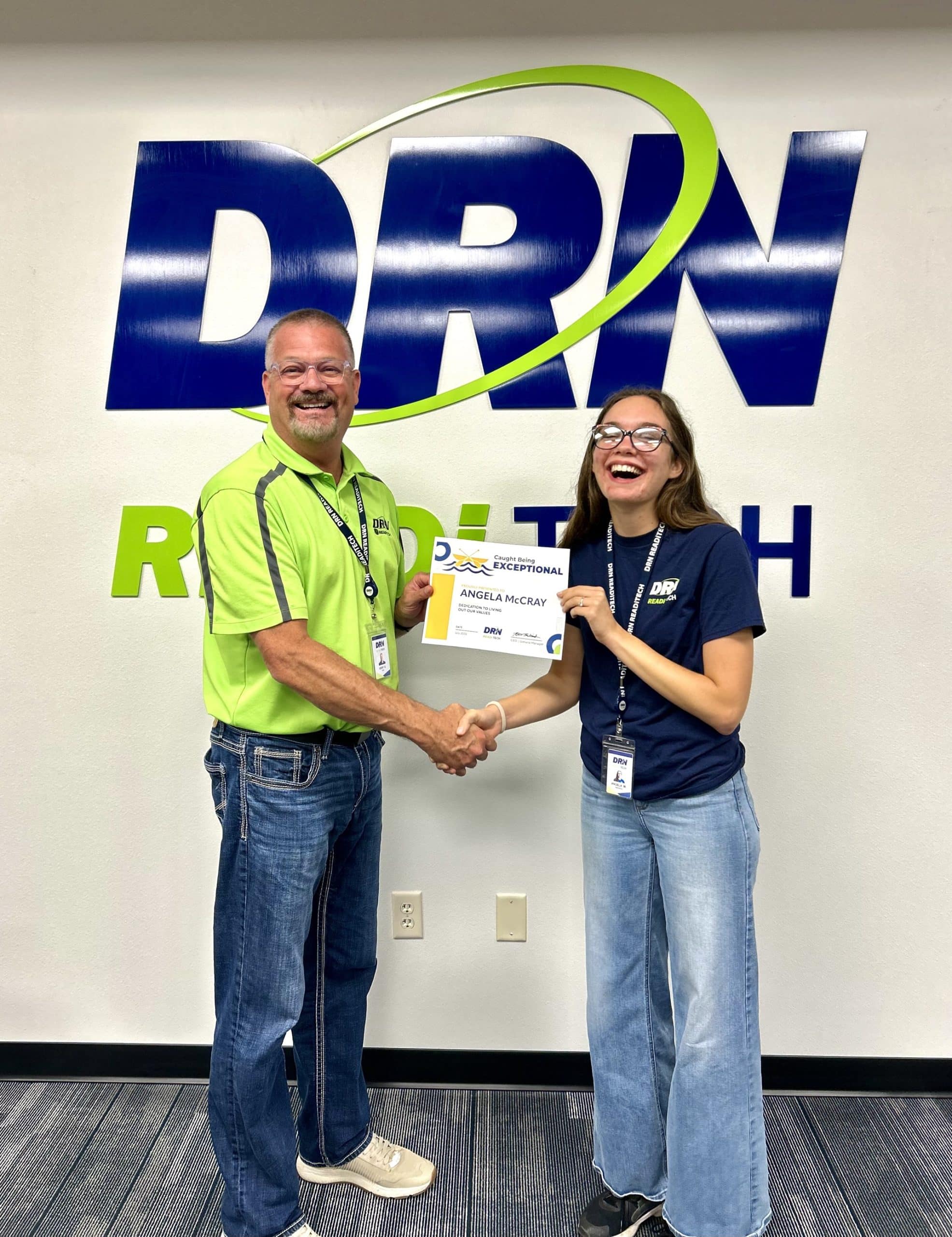 CEO Kent and Marketing Specialist Angela shake hands with award certificate.